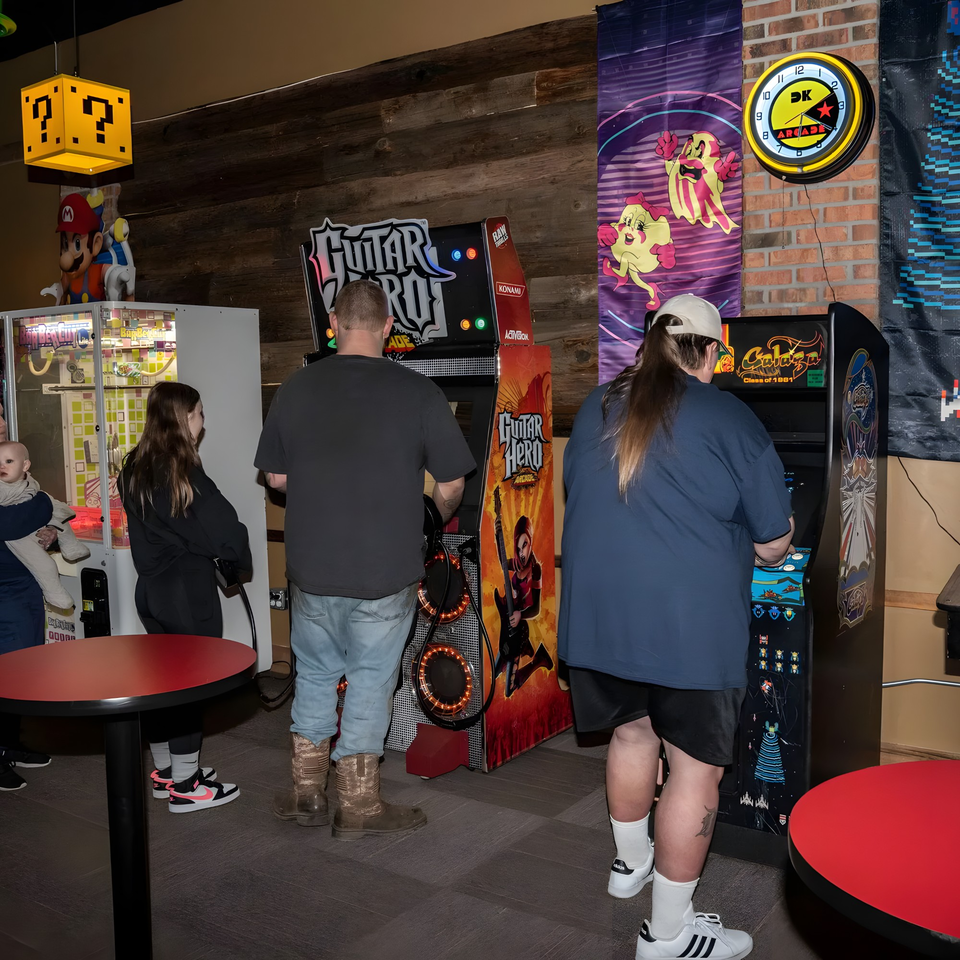 Patrons playing Guitar Hero and Galaga arcade games at The Pickled Goat Bar & Grill.