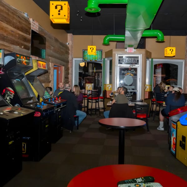 The Pickled Goat Bar & Grill's interior with arcade games, patrons dining, and Super Mario Bros. decor.