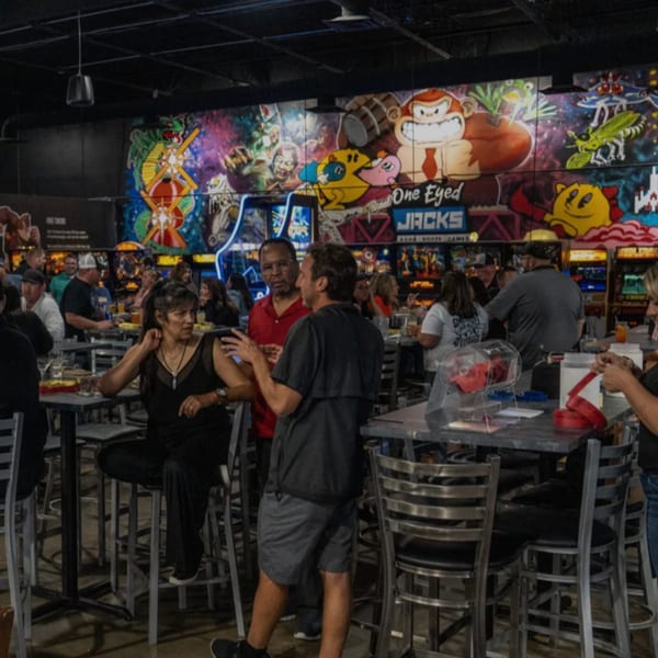 Patrons socialize at high-top tables in The Pickled Goat Bar & Grill, with arcade game murals in the background.