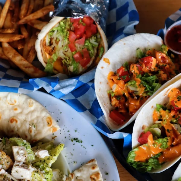 A bar and grill meal featuring tacos, a gyro, french fries, and a side salad.