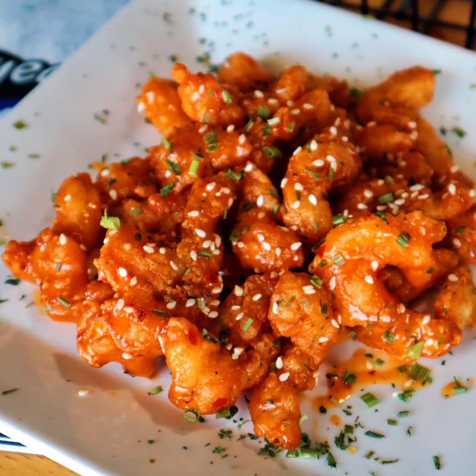 A plate of The Pickled Goat's crispy orange chicken, garnished with sesame seeds and green onions.