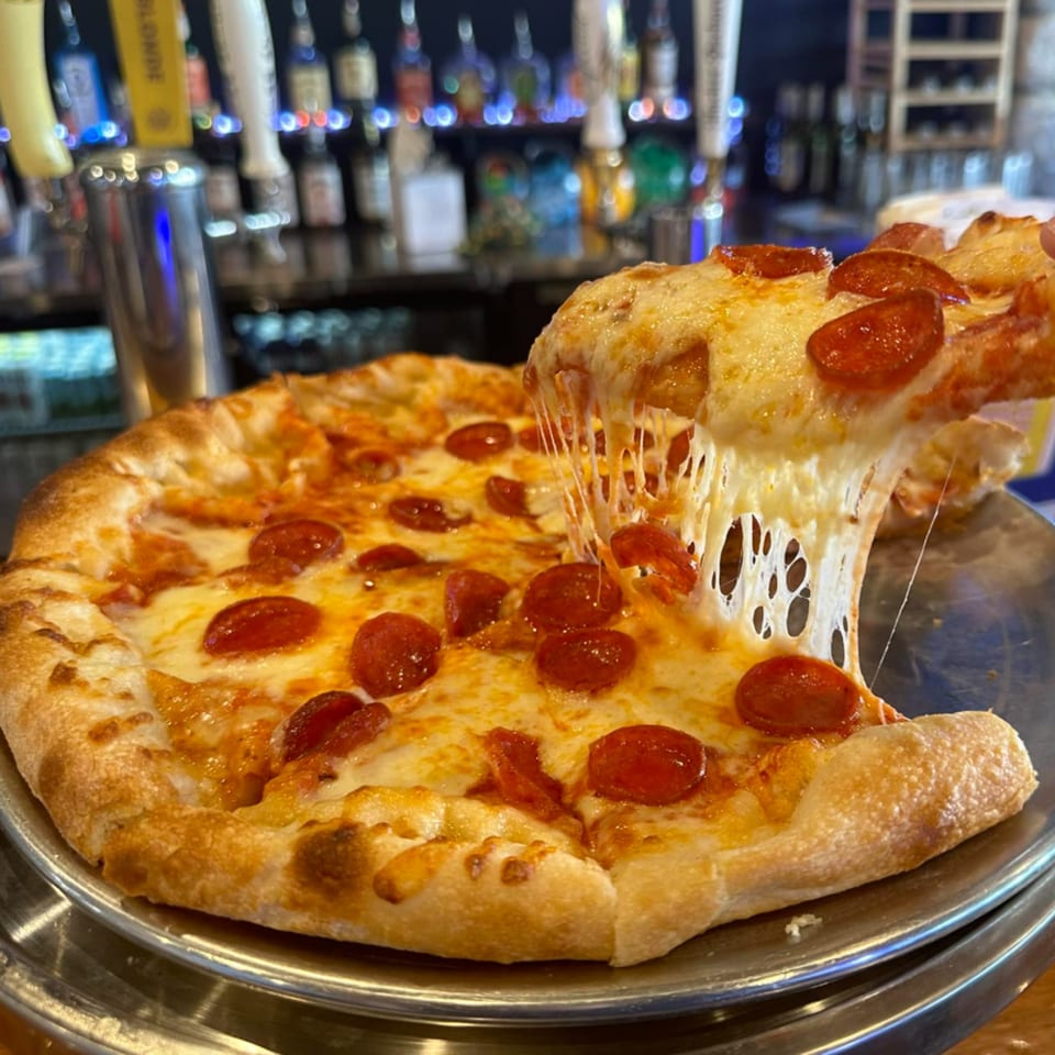 A pepperoni pizza with a slice being pulled, showing melted cheese, at The Pickled Goat Bar & Grill.