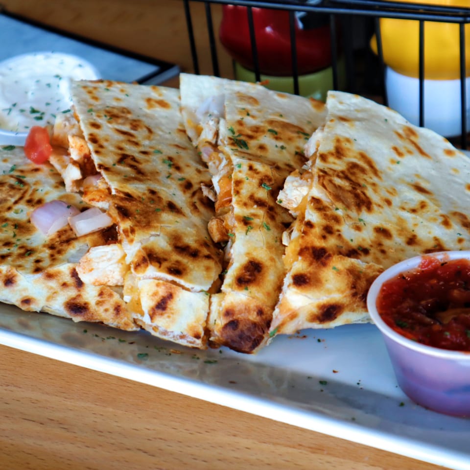 Golden-brown quesadilla wedges with chicken, onions, and tomatoes, served with salsa and sour cream.