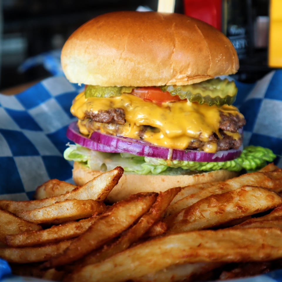 A double cheeseburger with lettuce, onion, tomato, and pickles, served with a side of fries.