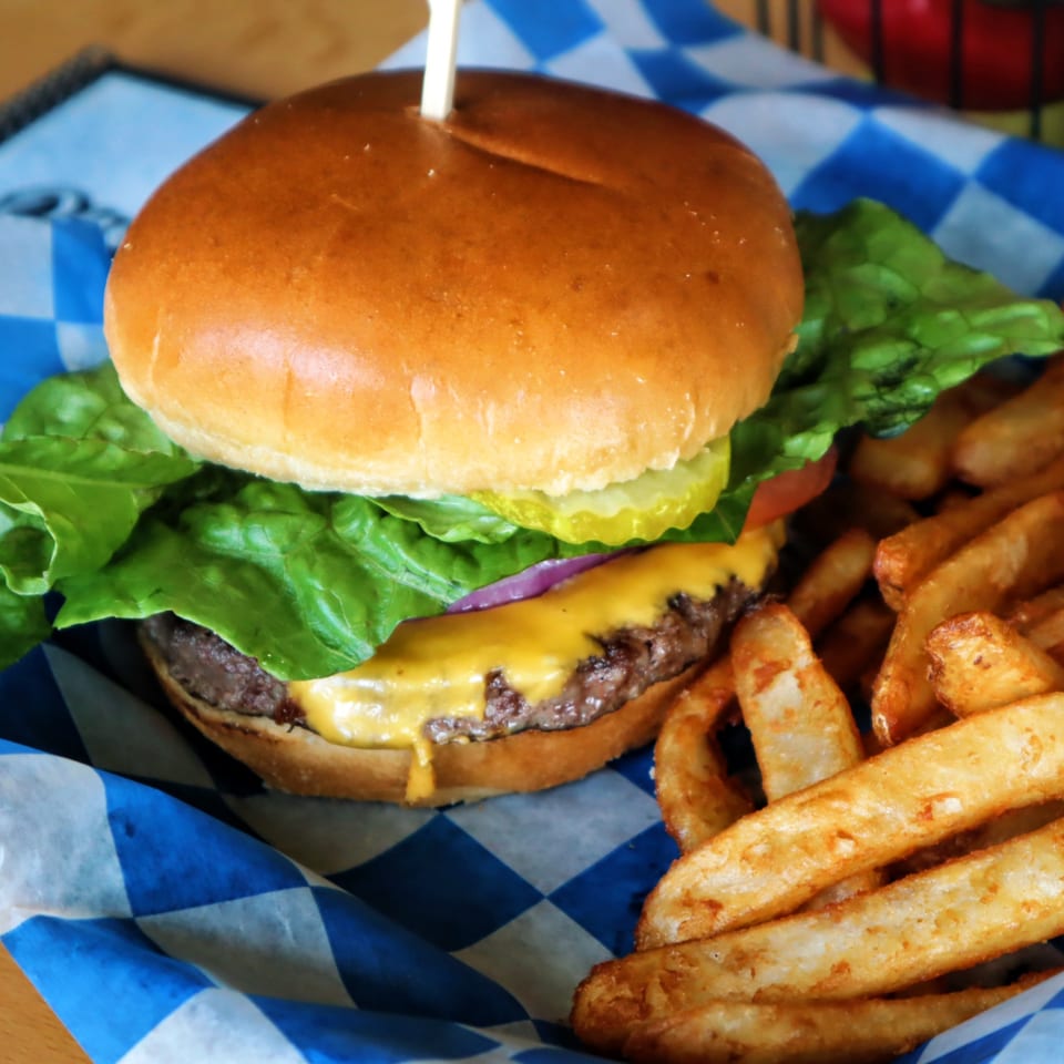 Cheeseburger with lettuce, tomato, onion, and pickles, served with thick-cut fries in a blue checkered basket.