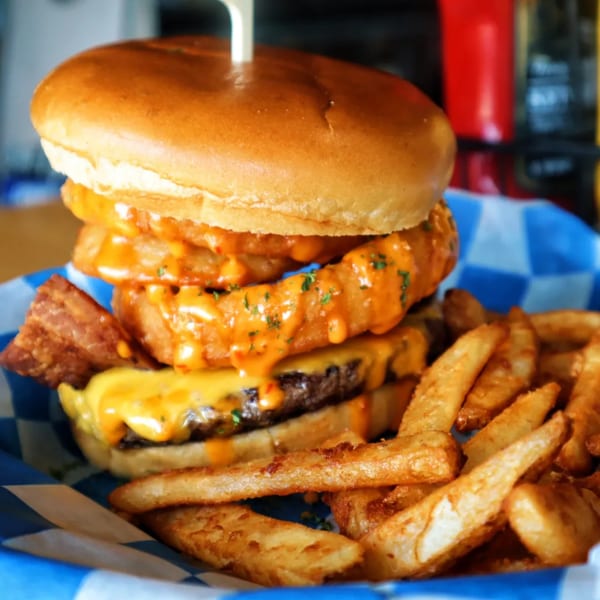 A Pickled Goat burger with onion rings, bacon, cheese, and fries in a blue checkered basket.
