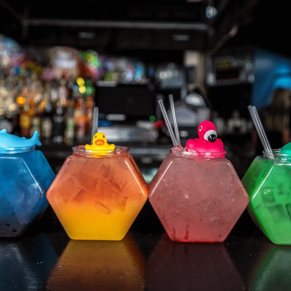 Four colorful, hexagonal drinks with novelty animal lids and straws on a bar top.