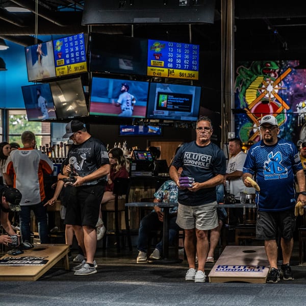 Patrons playing cornhole at The Pickled Goat Bar & Grill, with multiple TVs showing sports and Keno.