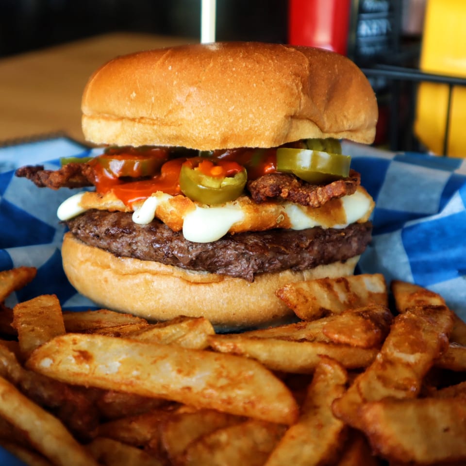 A Pickled Goat burger with jalapeños, bacon, and cheese, served with a side of fries.